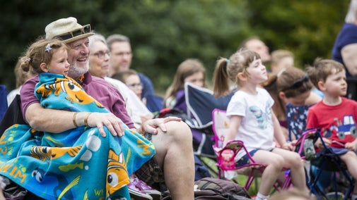 An audience enjoying an outdoor theatre event with an older man and young child in the foreground